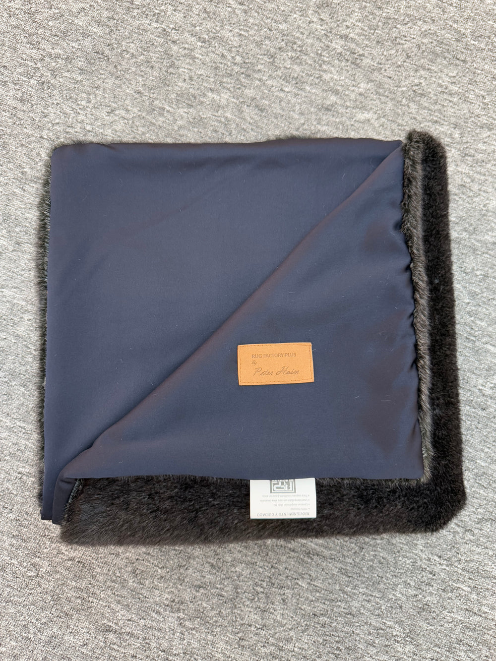 Folded navy blanket with black trim on a gray surface