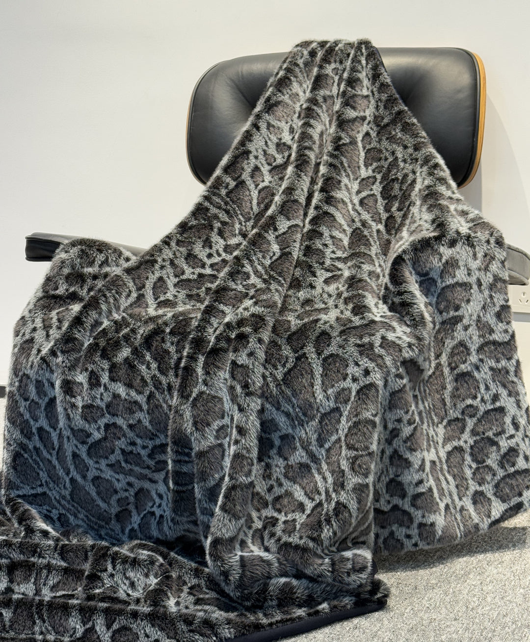 Gray leopard print blanket draped over a chair on a light gray background