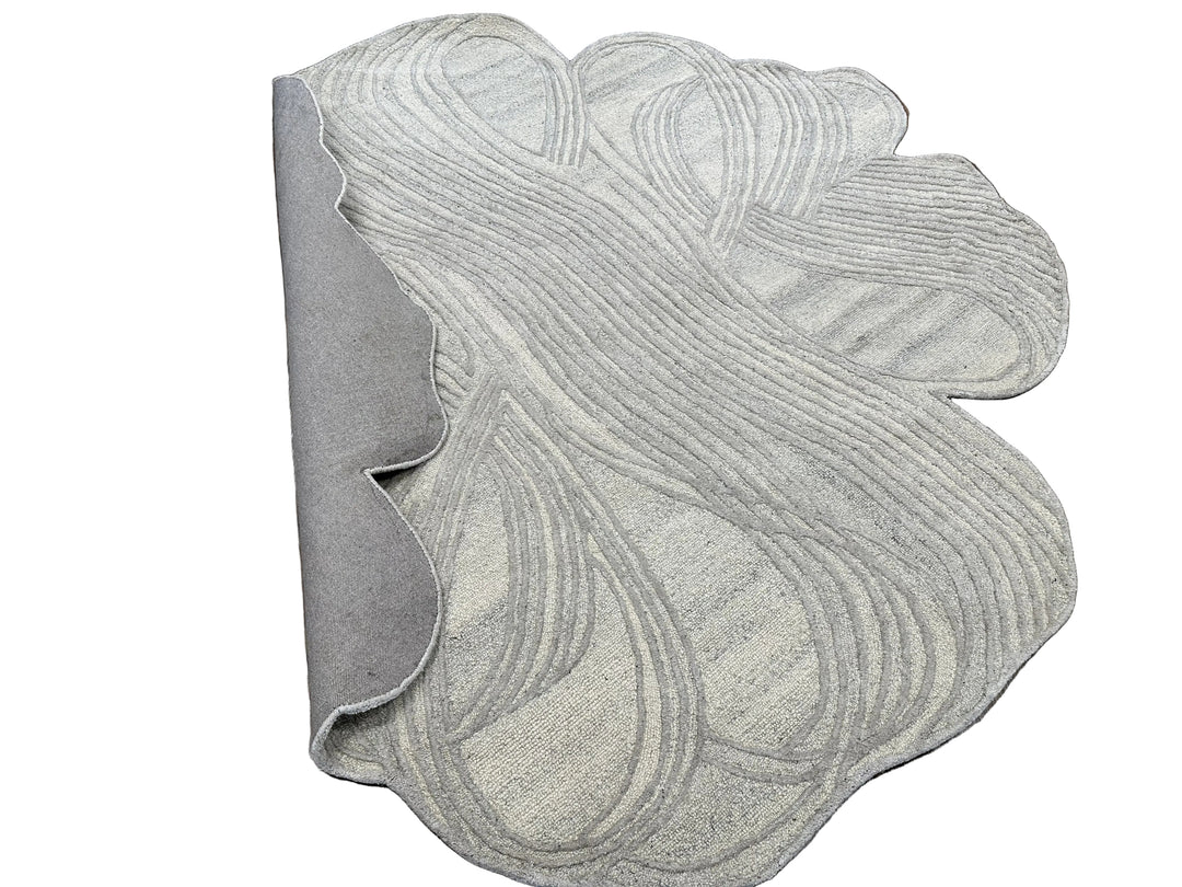 A light gray textured rug with an abstract wavy pattern, shown partially rolled to reveal its underside on a white background.