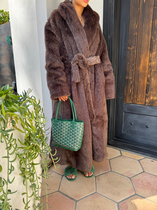Brown plush robe with green textured bag on a white surface near a wooden door and tiled wall.