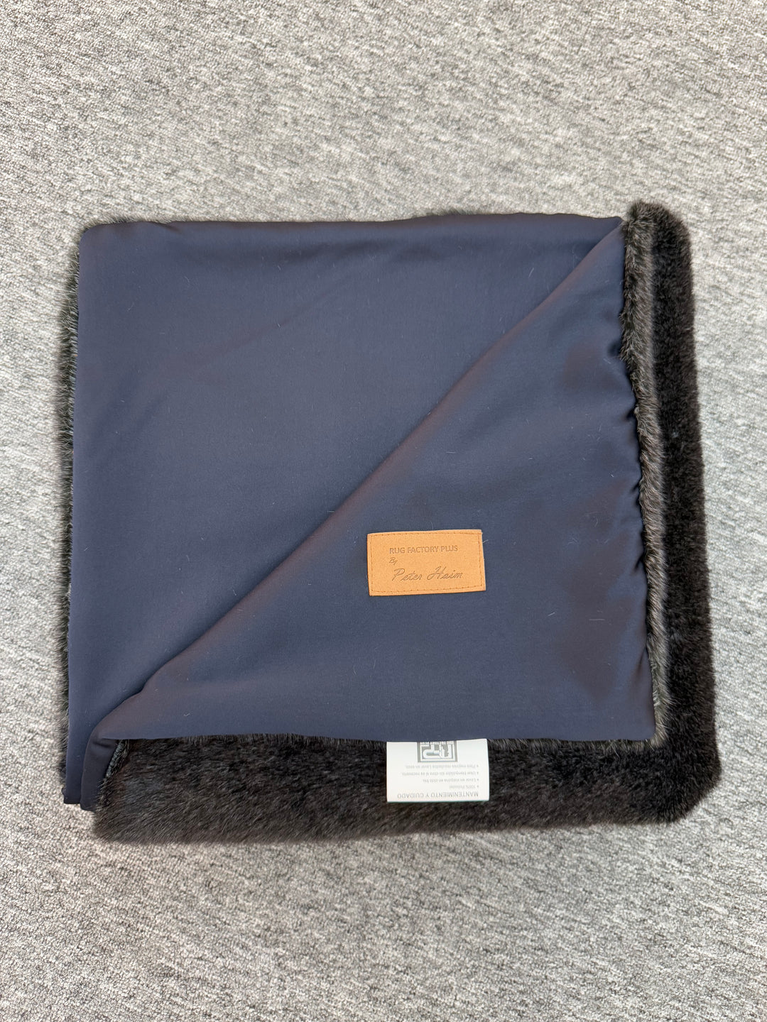 Folded navy blanket with black trim on a gray surface
