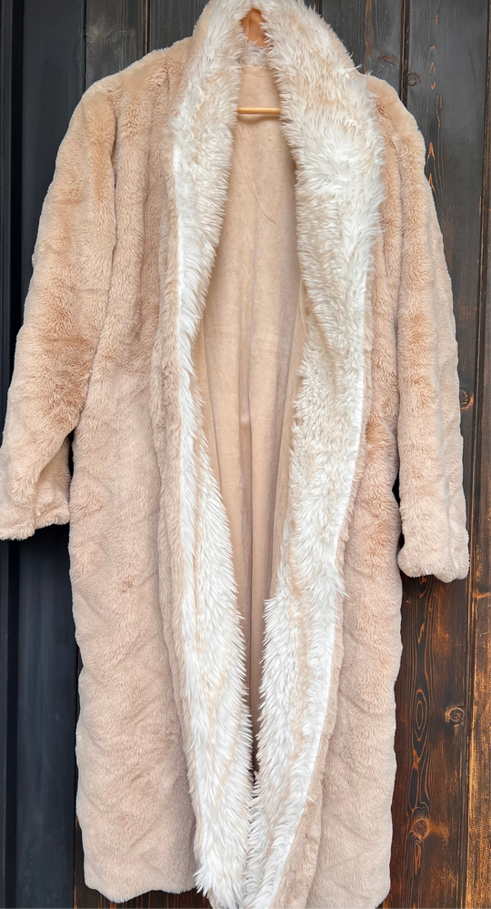 Beige fur coat with a white fur trim on a wooden hanger against a dark wooden background.