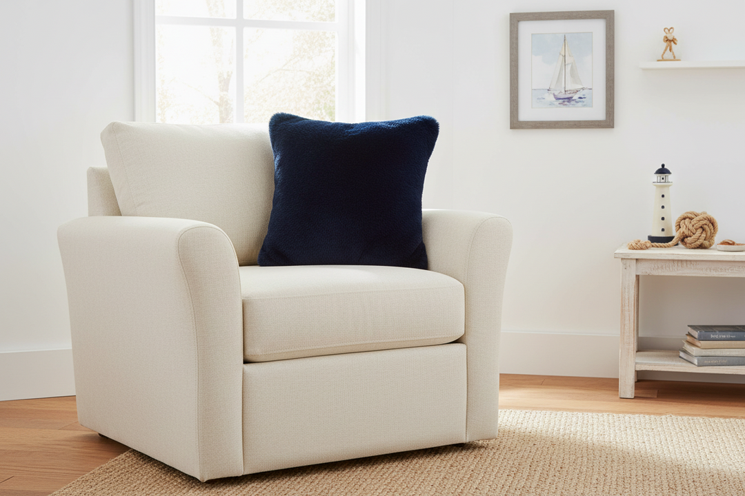 White armchair with a dark indigo pillow in a room with a window and shelf.
